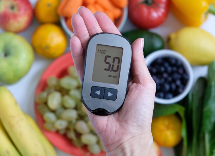 Frutas y verduras en el fondo y una mano con un medidor de azúcar